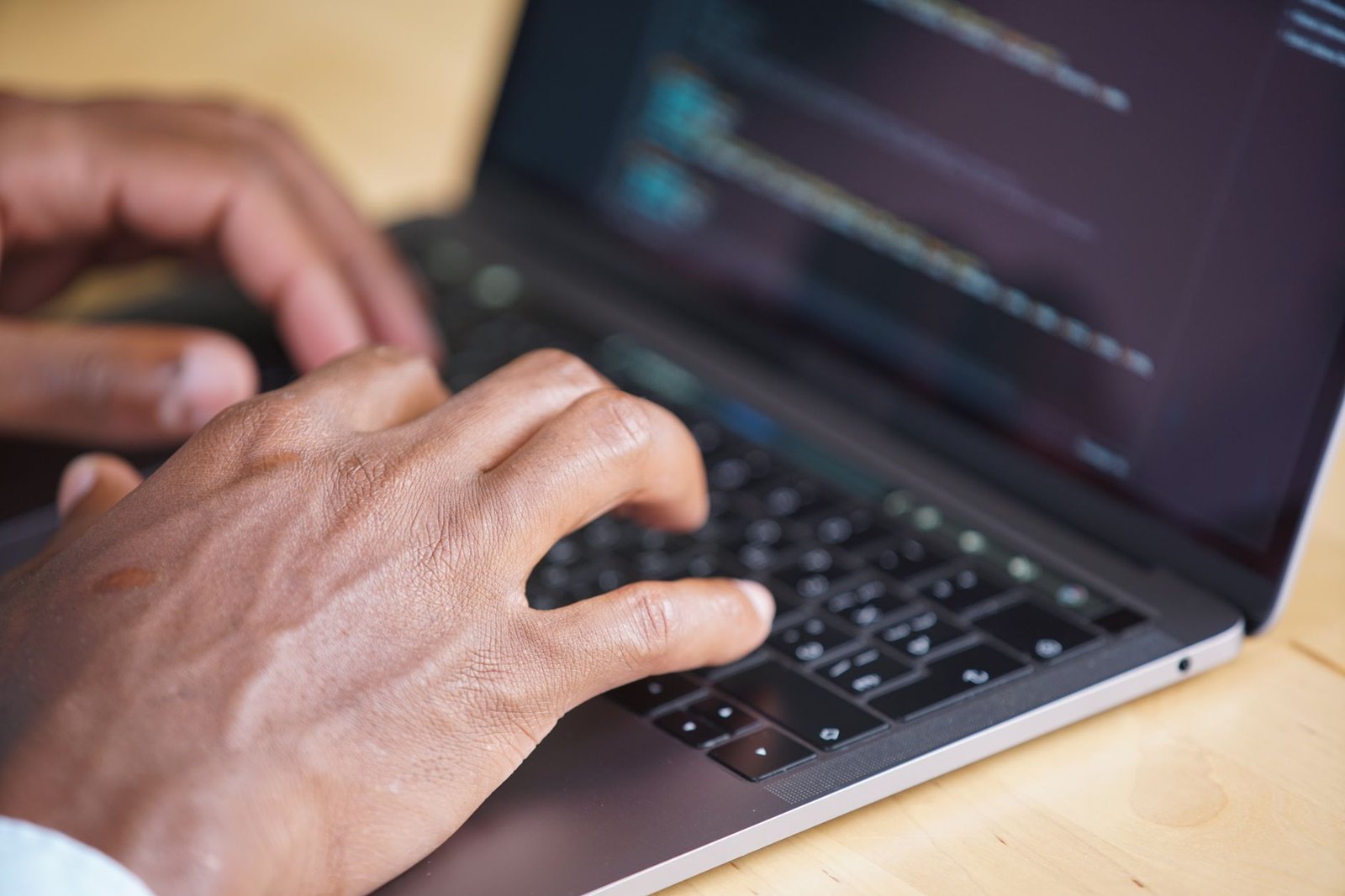 Close-up of hands typing on a computer keyboard with lines of code visible on the monitor.